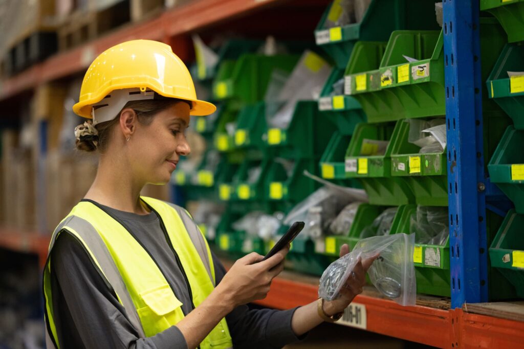 Frau mit Schutzhelm und Sicherheitsweste verwendet Etiketten Drucker für die Organisation von Lagermaterialien