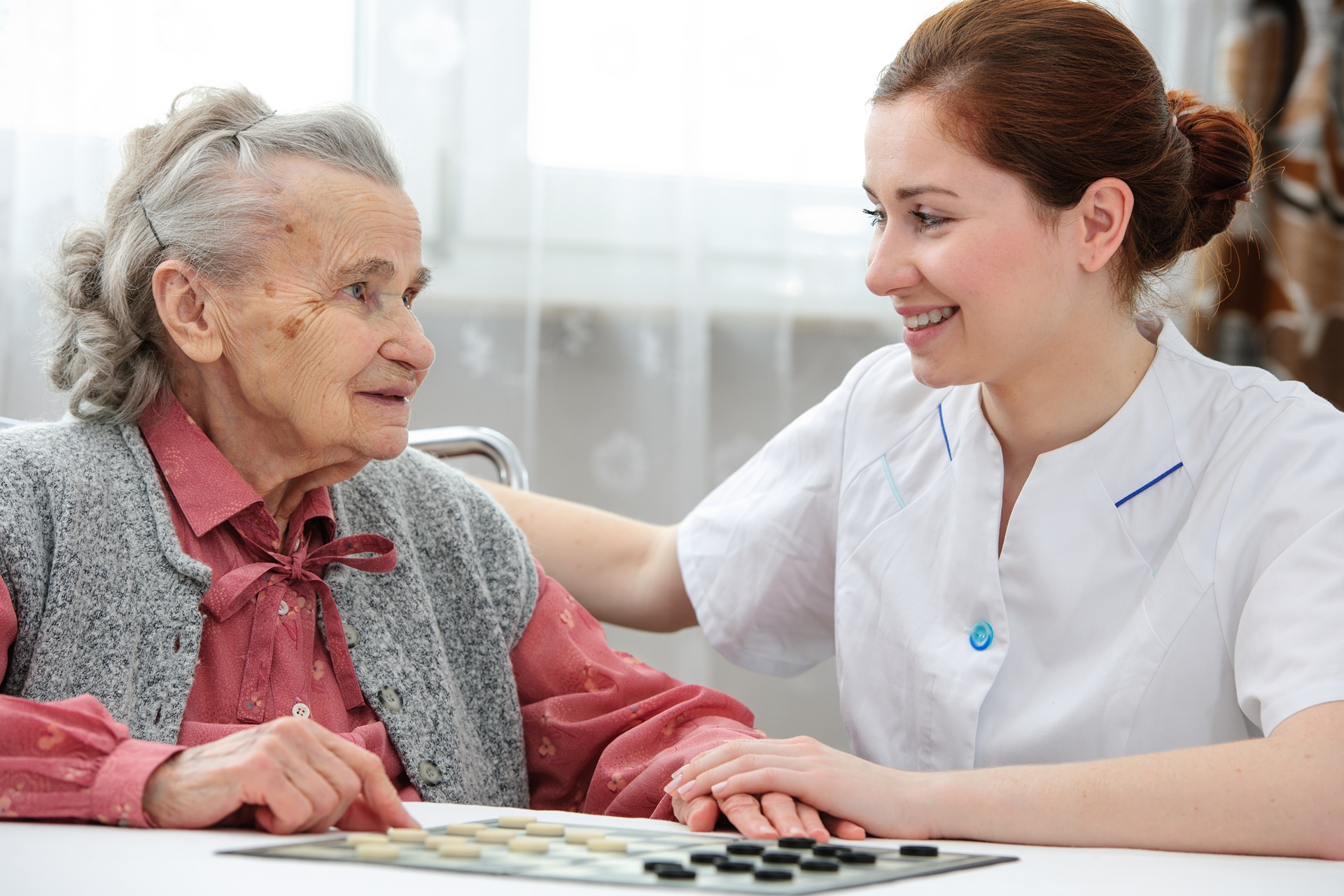 Pflegekraft im Spiel mit Seniorin am Tisch | Pflegehelfer Frankfurt

